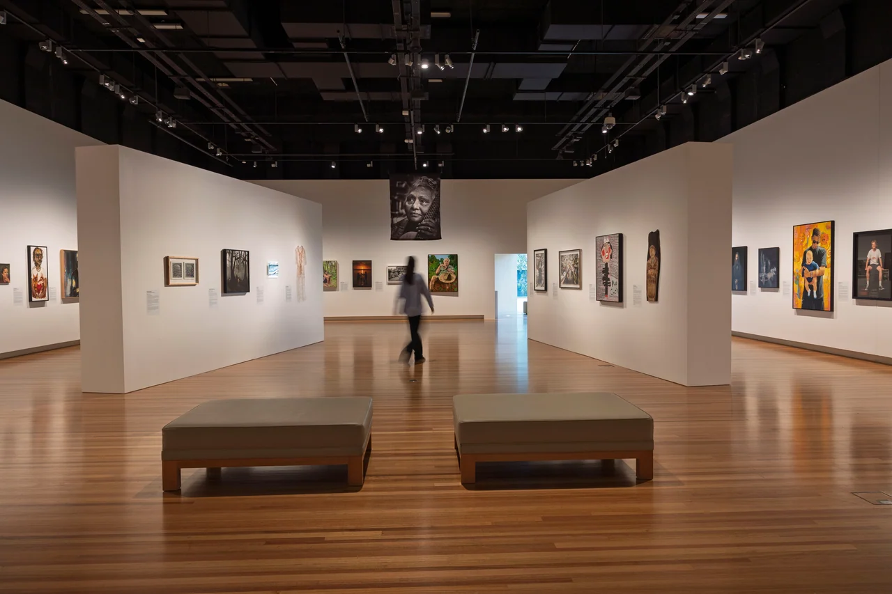 A visitor walks through the Brisbane Portrait Prize exhibition among paintings and photographs
