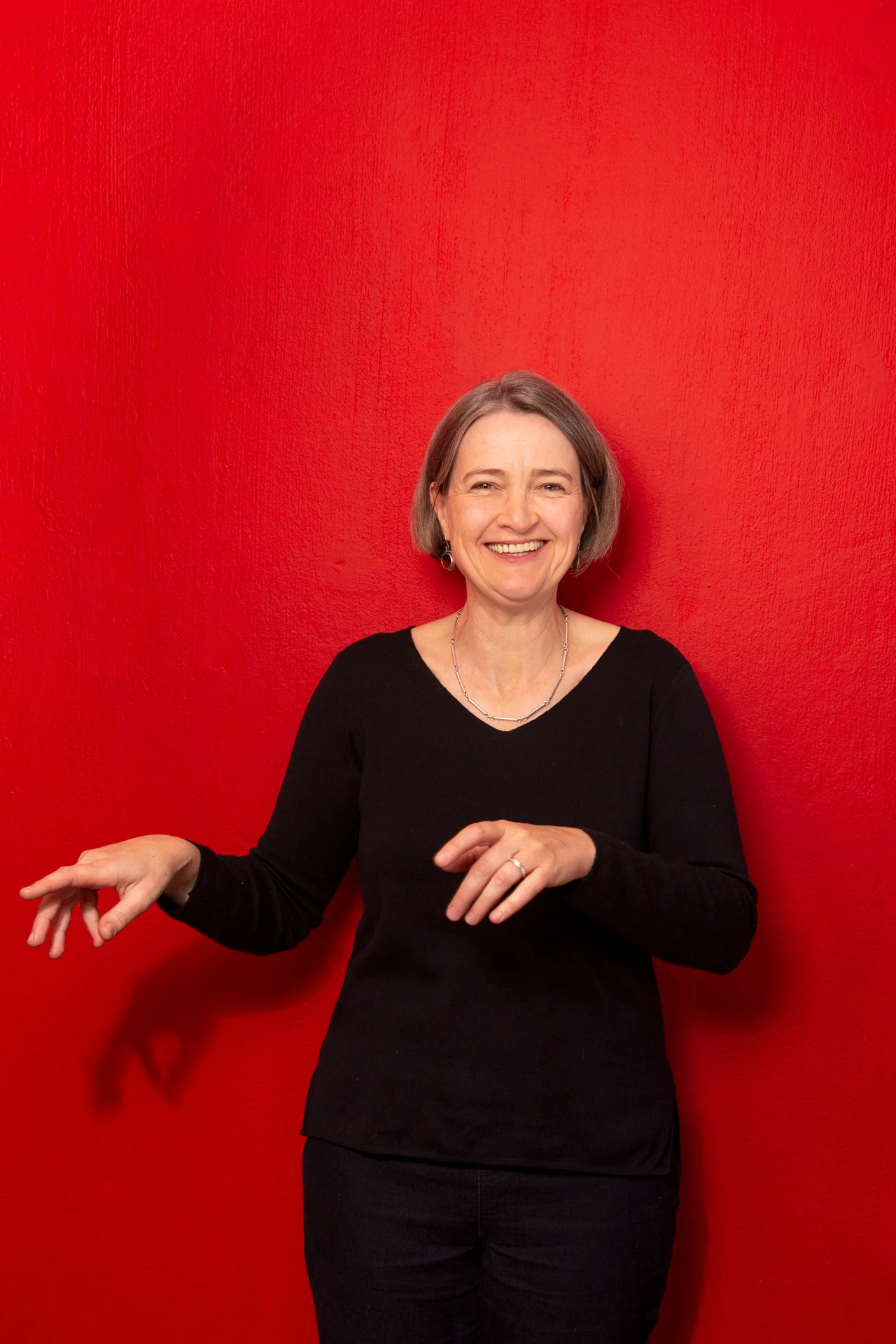 Clare Loveday smiling and gesturing in front of a vibrant red wall